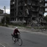 ESCOMBROS. Una mujer mayor pasa en bicicleta junto a los restos de un edificio de apartamentos cerca de Kiev.